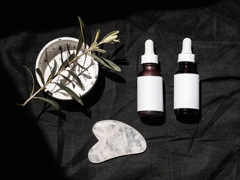 Two serum bottles with droppers, a bowl and an olive sprig on dark linen