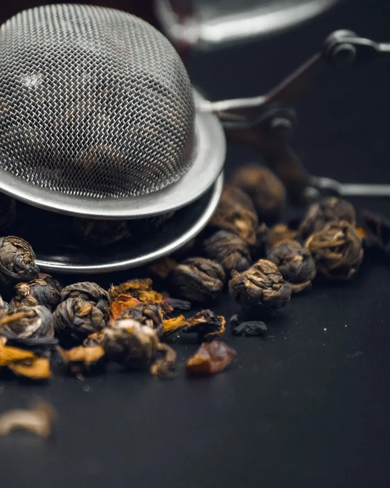 Rolled tea leaves and a metal strainer on a dark table