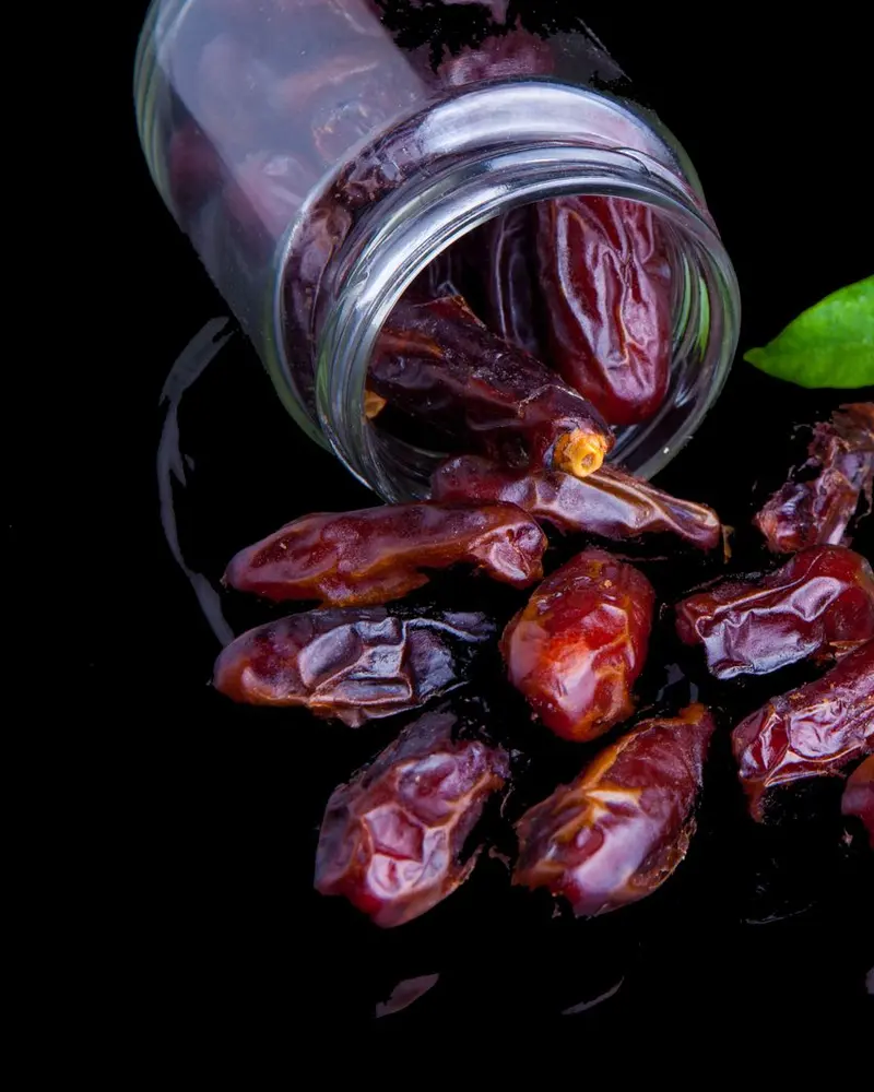 Dates spilling from a glass jar, with green leaves